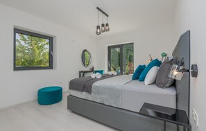 Relax in this serene bedroom with a large bed, a bedside table, and a balcony offering a view of the surrounding trees.