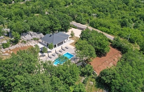 Surrounded by lush greenery, this house offers a patio with lounge chairs and a swimming pool.