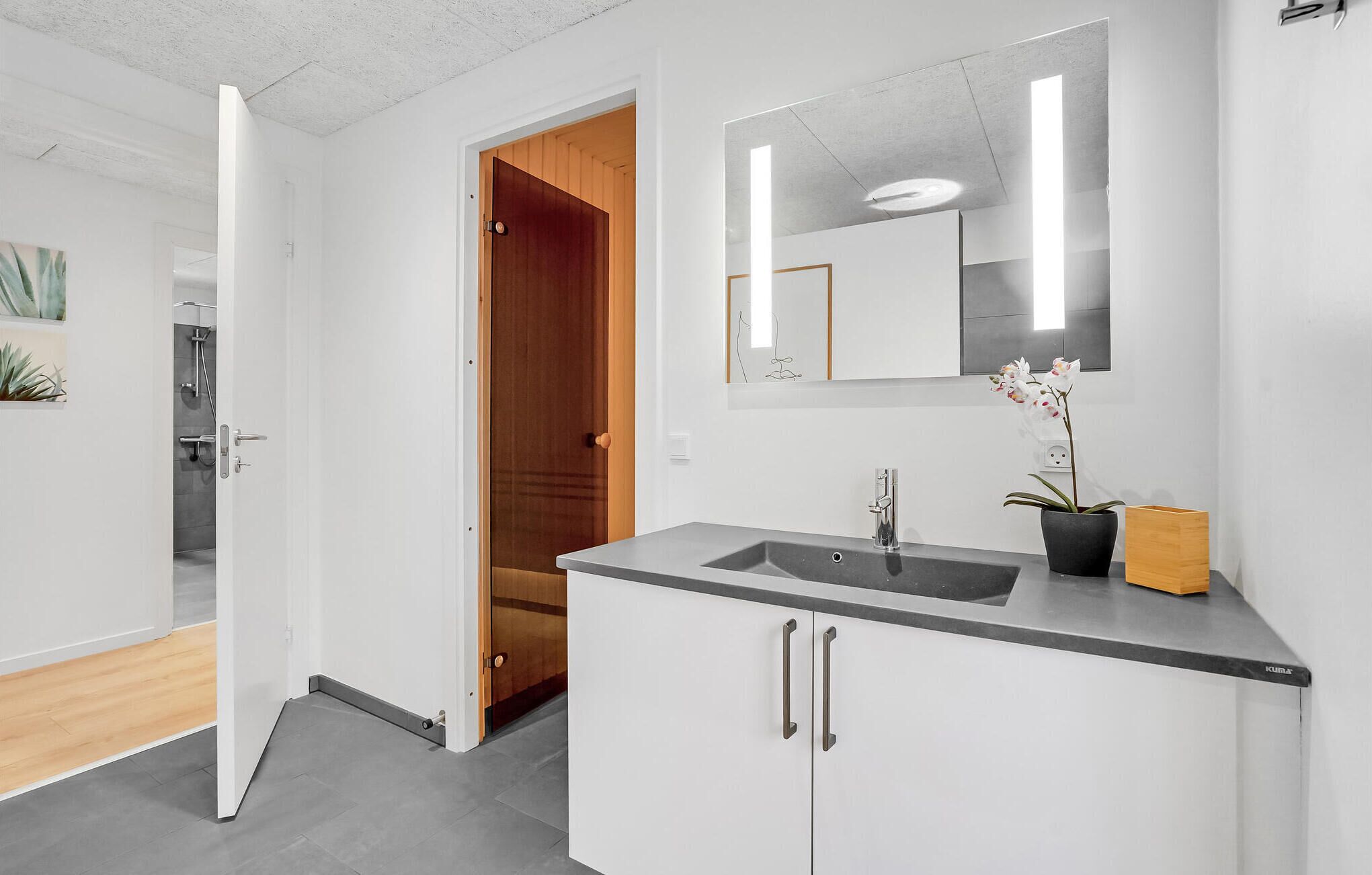 A modern bathroom with a grey sink, a mirror, and a wooden door leading to a shower area.