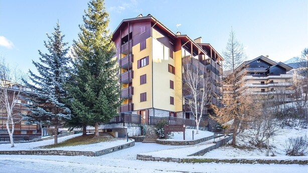Un hotel de varios pisos con balcones, un camino de piedra y alrededores nevados.