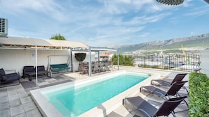 A rooftop pool area with a view of a mountainous landscape, a covered seating area, and a grill.