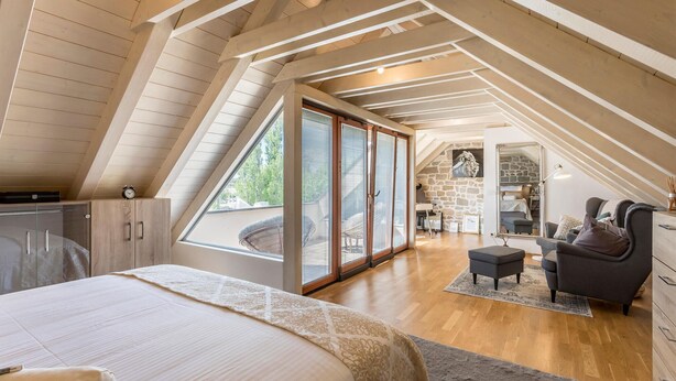 A bedroom with a large bed, a wardrobe, and a view through a glass door to a living area with a sofa and a chair. - Stunning home in Solin (Solin)