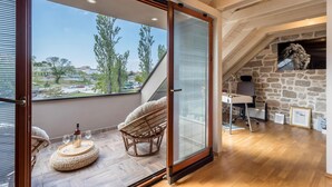 A room with a large sliding glass door leading to a balcony, a stone wall, a wooden ceiling, and a desk with a chair. - Stunning home in Solin (Solin)