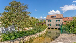 A stone building with a tiled roof, a narrow water channel, and lush greenery. - Stunning home in Solin (Solin)