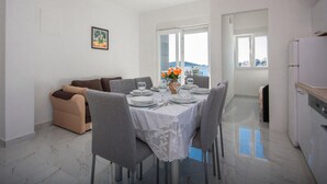 A dining area with a table set for six, grey chairs, a vase with orange flowers, and a painting on the wall. - Cozy apartment in Rogoznica with WiFi (Rogoznica)