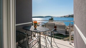 A balcony with a table and chairs, a vase with flowers, and a view of a body of water and distant hills. - Cozy apartment in Rogoznica with WiFi (Rogoznica)