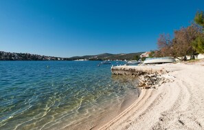 A clear beach with boats docked, a rocky shoreline, and a distant town. - Cozy apartment in Rogoznica with WiFi (Rogoznica)