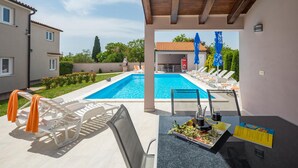 A poolside area with lounge chairs, a table with a drink and a menu, and a view of the pool and a building in the background. - Lovely home in Valtura (Valtura)