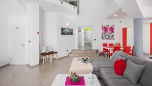 A spacious living area with a grey sofa, red accents, a dining area with red chairs, and a staircase leading to an upper level. - Lovely home in Valtura (Valtura)