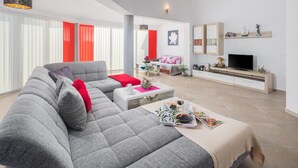 Een moderne woonkamer met een grijze modulaire bank, een salontafel met tijdschriften, een tv op een houten dressoir en een rode accentmuur.