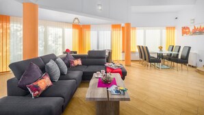 A modern living room with a sectional sofa, a dining table with chairs, and a large window with orange curtains. - Lovely home in Valtura (Valtura)