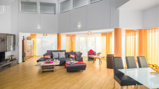 Een ruime woonkamer met een zithoek, een eettafel met stoelen en een televisie.