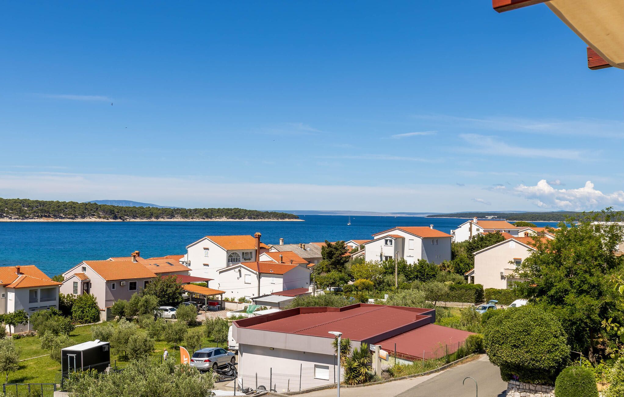 A coastal residential area with houses featuring red-tiled roofs, a clear blue sky, and a view of the sea.