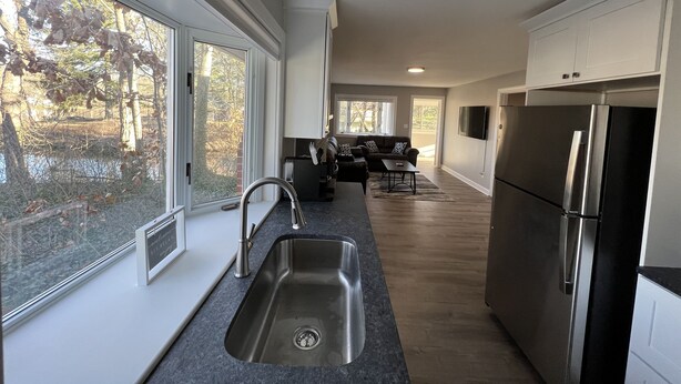A modern kitchen with a stainless steel sink, a refrigerator, and a dining area with a sofa and table. - The Lakeside Cottage in Stow! (Stow)