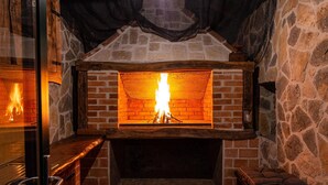 A stone fireplace with a fire burning inside, surrounded by stone walls and a wooden bench.