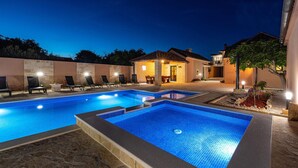 A swimming pool with lounge chairs and a covered seating area at dusk.