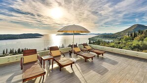 Terraza con mobiliario de madera y una sombrilla grande, con vista a un lago y colinas.