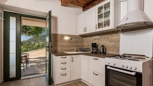 Une cuisine avec des meubles blancs, une cuisinière et une machine à café. On peut apercevoir un jardin à travers une porte ouverte.