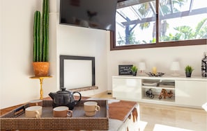 Un accogliente soggiorno con un'ampia finestra, un cactus, un quadro incorniciato, un servizio da tè e un mobiletto bianco con oggetti decorativi.