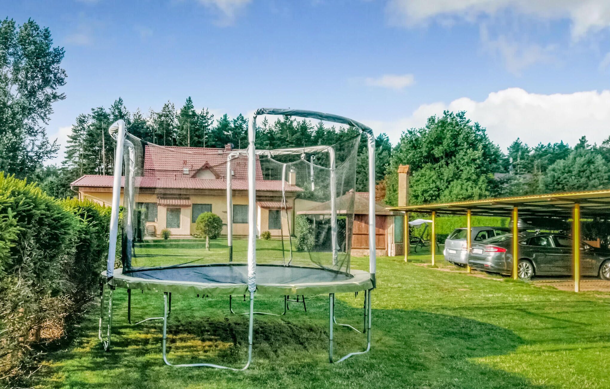 Un trampolino da giardino con una casa e auto parcheggiate sullo sfondo.