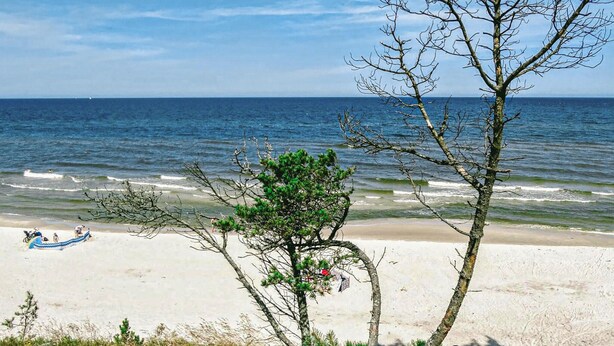 A beach with a clear view of the ocean, a few people, and a blue boat on the sand. - Beautiful apartment in Kopalino (Kopalino)