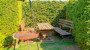 A wooden picnic table and bench set in a garden with a metal grill and umbrella. - Beautiful apartment in Kopalino (Kopalino)
