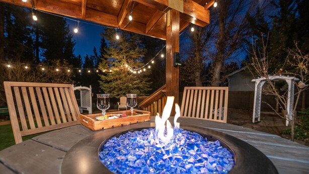 Un patio al aire libre con un brasero, sillas de madera y luces colgantes.