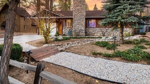 Una cabaña rústica con chimenea de piedra, una terraza de madera y un camino de grava.
