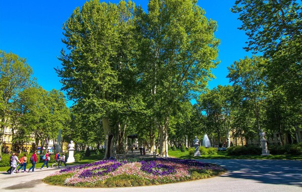 A park with a large tree, statues, and a flower bed.