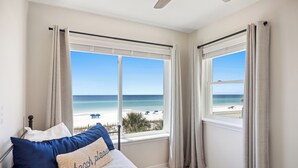 A bedroom with a bed, a view of the beach, and a window with curtains. - 5 STAR BEACH FRONT RENOVATED TOWNHOME with BEACH SERVICE on Okaloosa Island (Fort Walton Beach)