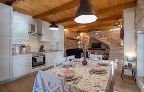 A modern kitchen with white cabinets, a wooden ceiling, and a dining area with a floral tablecloth. - Lovely home in Glavina donja (Glavina donja)