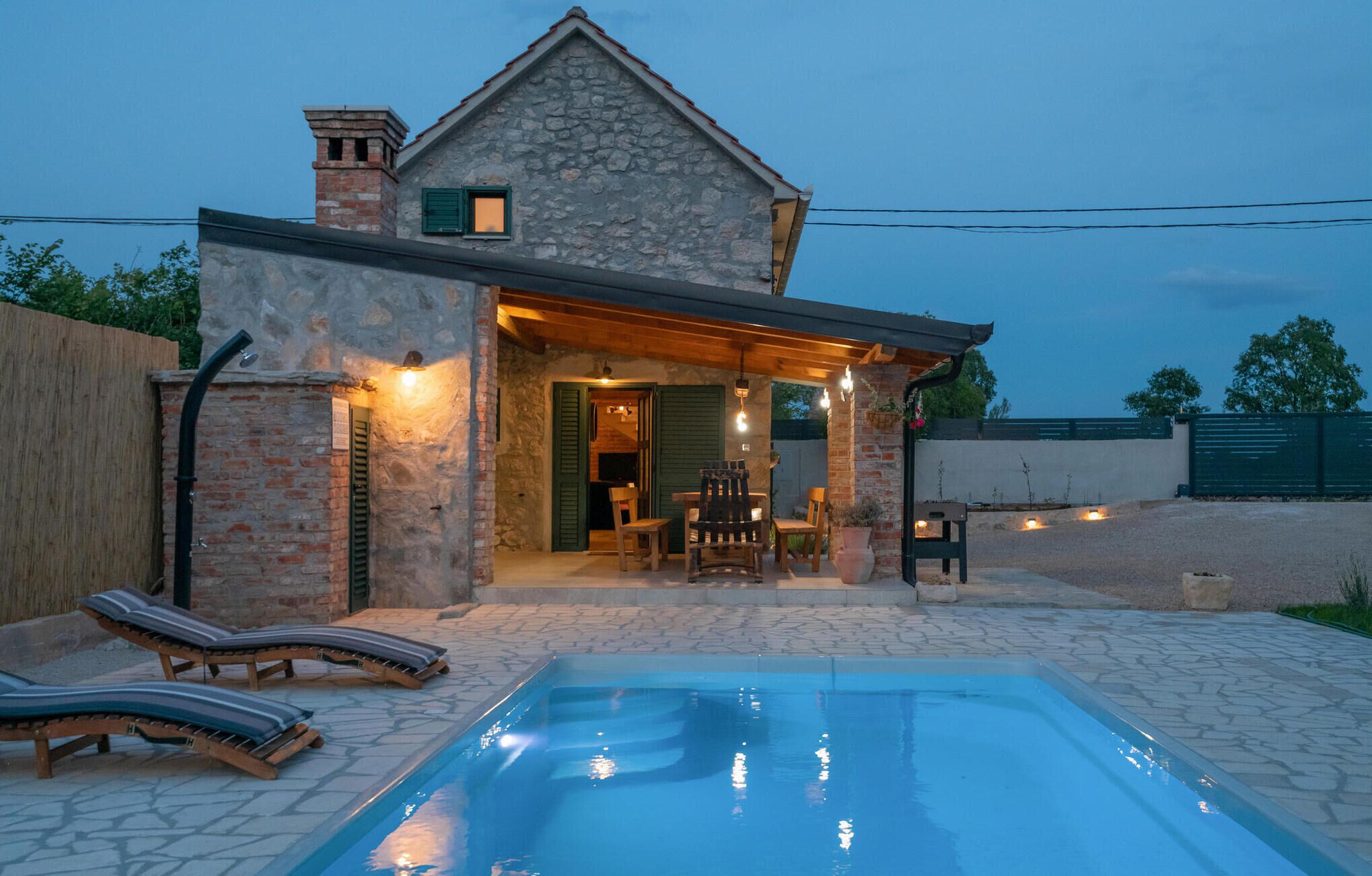 Een stenen huis met een zwembad, terras en een overdekte patio.