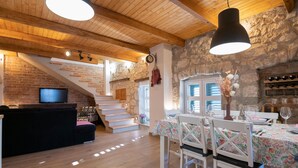 A cozy interior with a wooden staircase, a dining area with floral tablecloths, and a stone wall. - Lovely home in Glavina donja (Glavina donja)