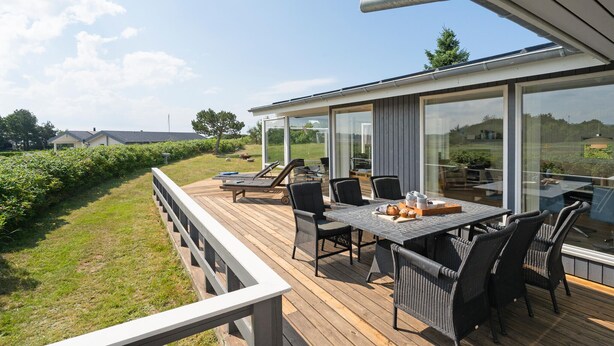 A deck with a table and chairs, overlooking a grassy area with a view of the countryside.