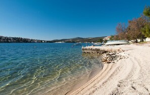 Una playa despejada con barcos, una costa rocosa y un pueblo lejano.