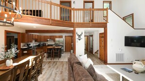 A spacious living area with a wooden staircase, a dining table with chairs, a sofa, and a television. - Whiskey Ridge - Luxury Mountaintop Family Retreat * Dog Friendly * Hot Tub (Wintergreen Resort)
