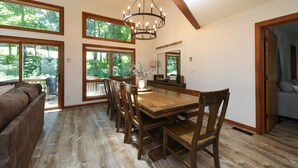 A dining area with a wooden table and chairs, large windows, and a chandelier. - Whiskey Ridge - Luxury Mountaintop Family Retreat * Dog Friendly * Hot Tub (Wintergreen Resort)