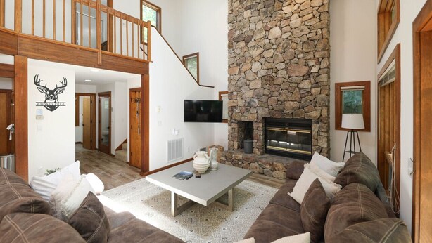 A spacious living room with a stone fireplace, a high ceiling, and a wooden staircase. - Whiskey Ridge - Luxury Mountaintop Family Retreat * Dog Friendly * Hot Tub (Wintergreen Resort)