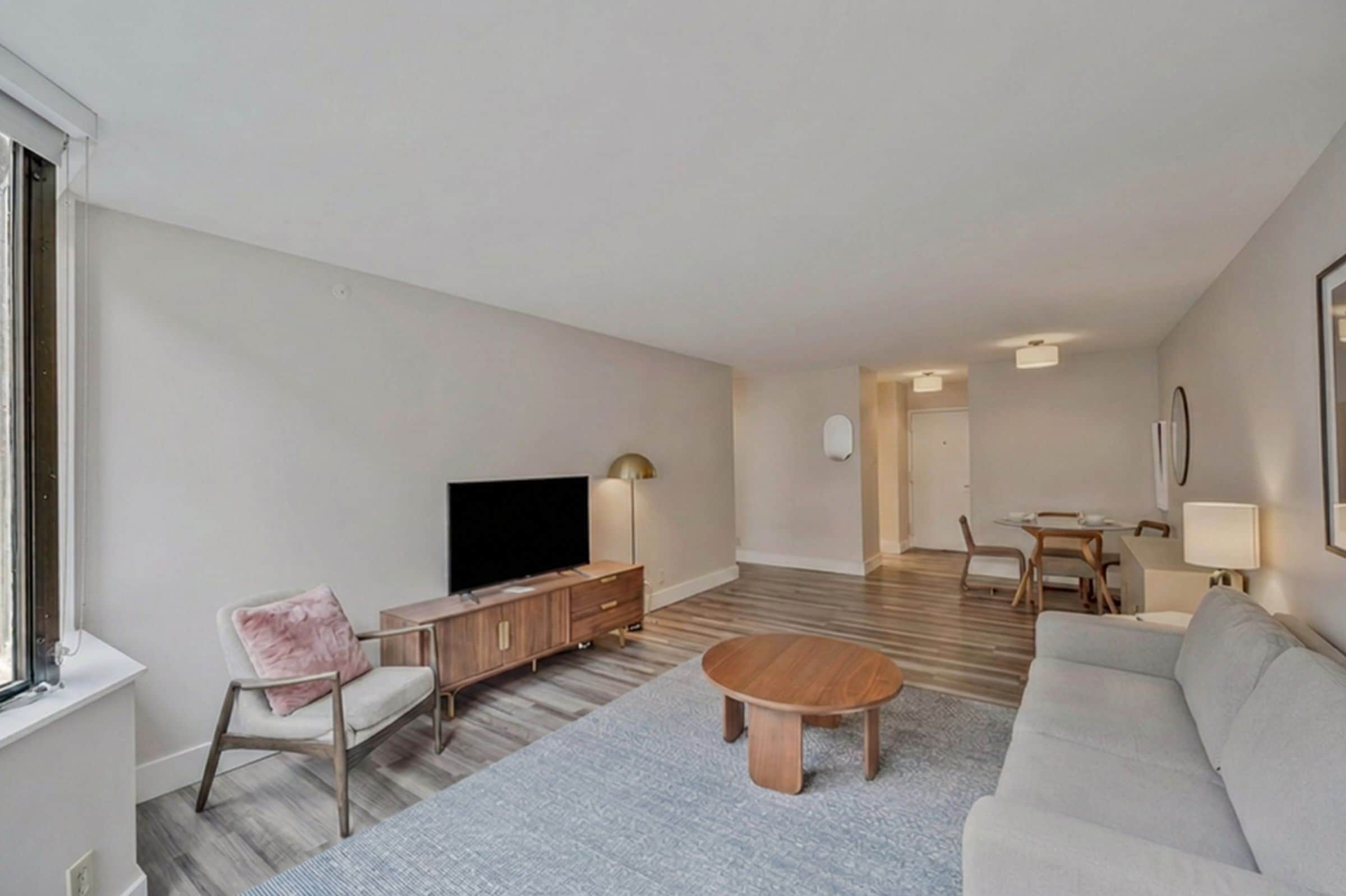 A modern living room with a flat-screen TV, a sofa, a coffee table, and a dining area with a table and chairs.