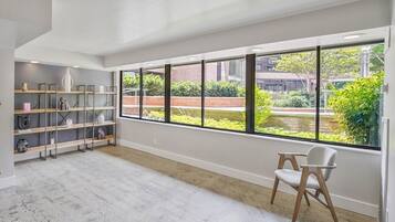 A spacious room with a large window, a chair, and a shelving unit with various decorative items.