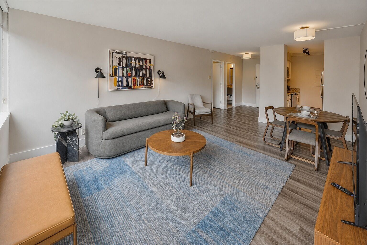 Un salon moderne avec un canapé gris, une table basse ronde et un coin repas comprenant une table et des chaises en bois.