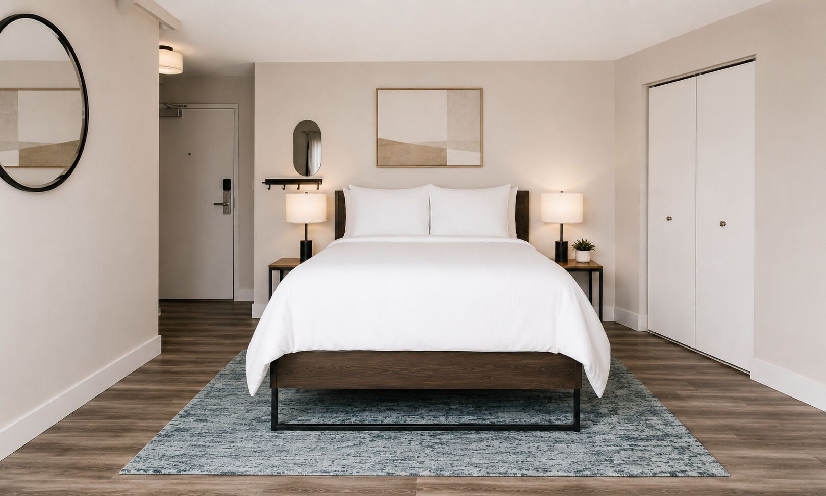 Moderni hotellihuone, jossa on suuri sänky, kaksi yöpöytää valaisimineen, peili, kehystetty taideteos ja vaatekaappi.