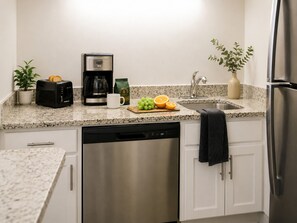 A kitchen with a coffee maker, toaster, sink, and a dish rack.