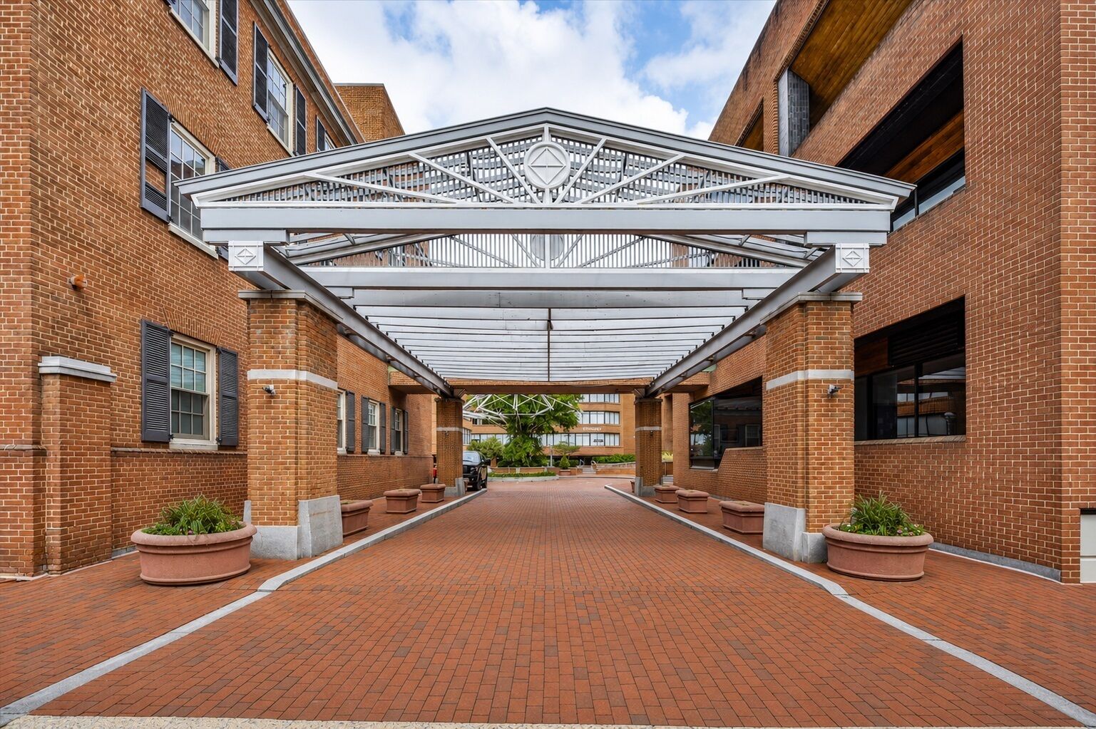 A covered walkway between brick buildings with planters and a central walkway.