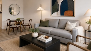 A modern living room with a grey sofa, a round coffee table, and a dining area with wooden chairs and a glass table. - Global Luxury Suites at Georgetown (Washington)