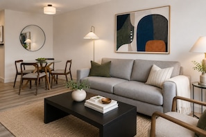 Un salon moderne avec un canapé gris, une table basse ronde et un coin repas comprenant des chaises en bois et une table en verre.