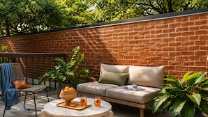 A patio area with a brick wall, a sofa, a chair, a table with a bowl of fruit, and potted plants. - Global Luxury Suites at Georgetown (Washington)