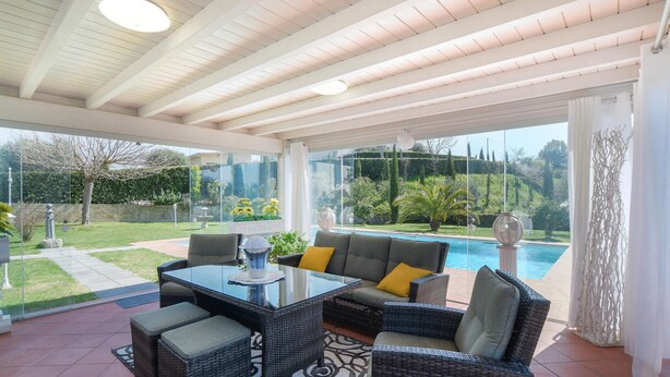 A covered patio area with wicker furniture, a glass table, and a view of a swimming pool and garden. - Cozy home in Fucecchio with WiFi (Fucecchio)