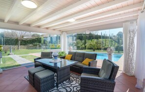 A covered patio area with wicker furniture, a glass table, and a view of a swimming pool and garden. - Cozy home in Fucecchio with WiFi (Fucecchio)