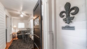 A hallway with a dining area featuring a table and chairs, a black door with a number plaque, and a decorative fleur-de-lis on the wall. - Historic Tremain  Cottages (Mount Dora)